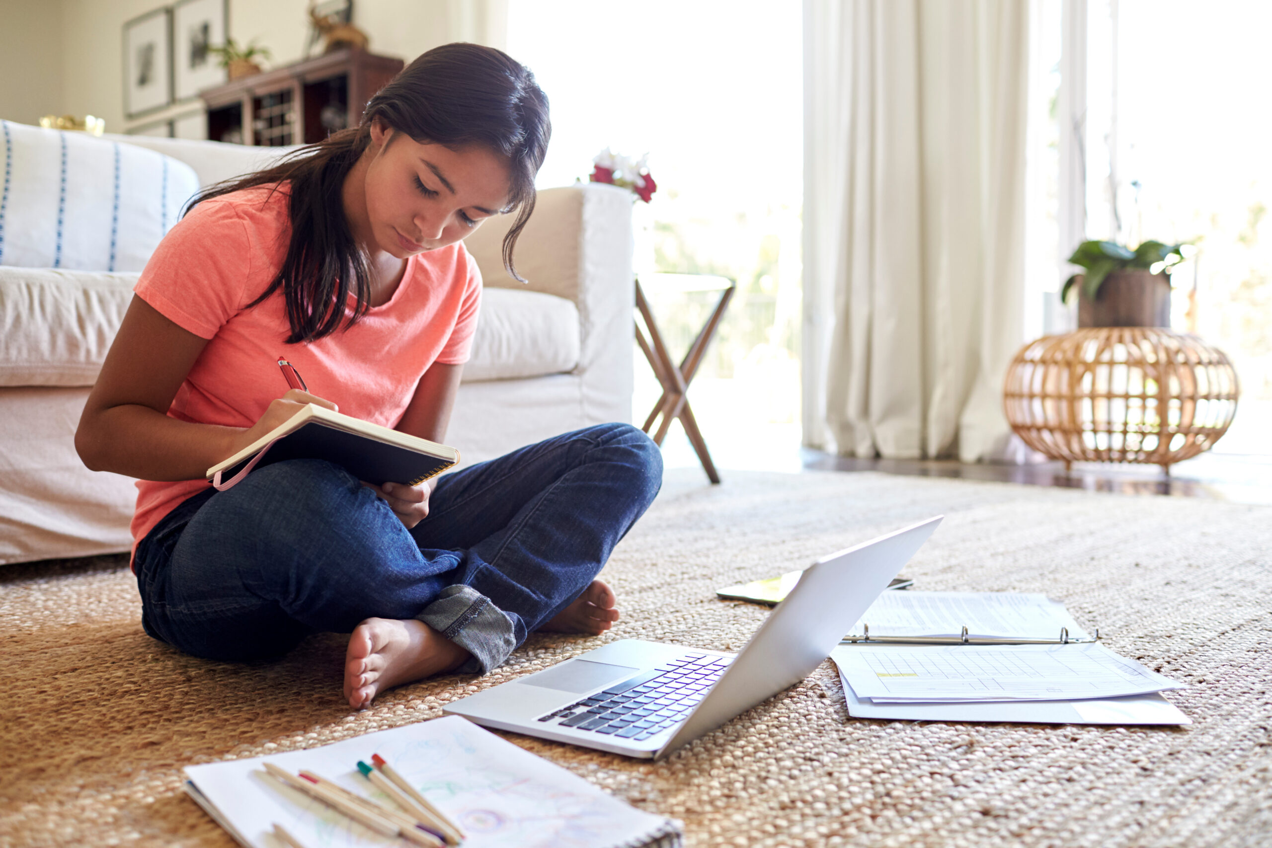 Teenage girl doing her homework sitting on floor in the living room, low angle, close up
